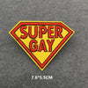 A yellow and red diamond shaped embroidered patch with the text SUPER GAY on a gray fabric background.