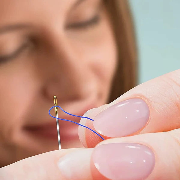 A hand is using a precision self-threading sewing needle kit to thread a blue thread onto a pink fingernail.