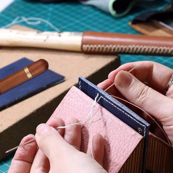 A hand is using a precision self-threading sewing needle kit to thread a needle inside a pink fabric box.