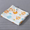 A white cotton muslin swaddle blanket featuring colorful geometric patterns in orange, yellow, and blue.