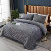 A gray crystal velvet quilted bedspread draped over a bed in a modern bedroom setting.