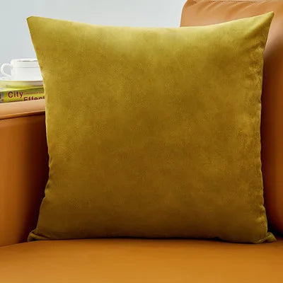 A square olive green velvet decorative cushion resting on an orange sofa.