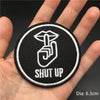 Black embroidered punk badge with a hand gesture and the text SHUT UP shown on a person's palm.