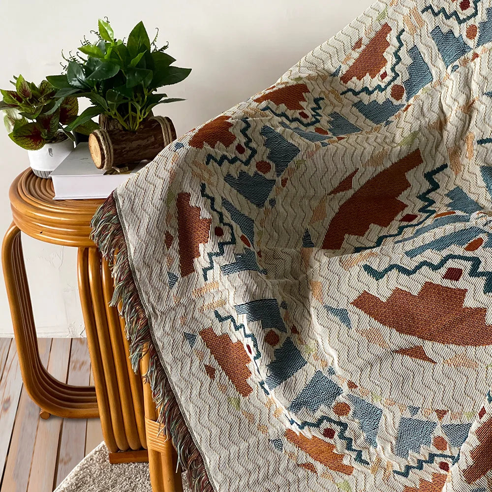 A close-up of a bohemian geometric throw blanket featuring earthy tones and blue patterns draped over a wooden stool.