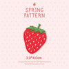 A pink background features a hand-stitched strawberry embroidery patch with green leaves and white seeds, labeled as a spring