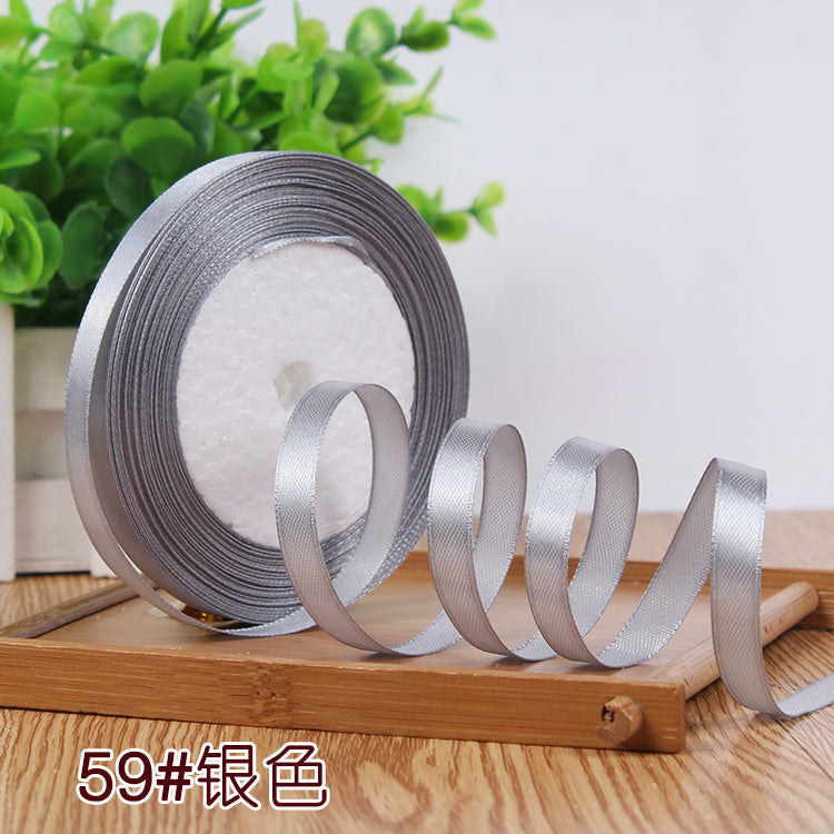 Roll of silver satin ribbon with a white core displayed on a wooden surface.