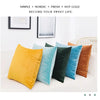 A collection of solid velvet decorative cushion covers in yellow, teal, dark green, and burnt orange arranged on a white sofa