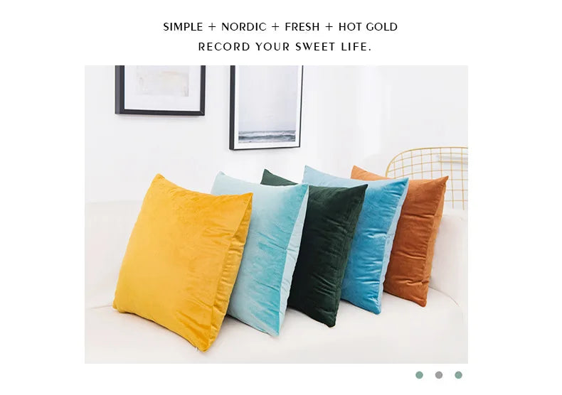 A collection of solid velvet decorative cushion covers in yellow, teal, dark green, and burnt orange arranged on a white sofa