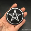 A hand holds a black embroidered punk badge featuring a white six-pointed star design.