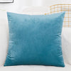 A solid teal velvet decorative cushion cover resting on a white sofa.