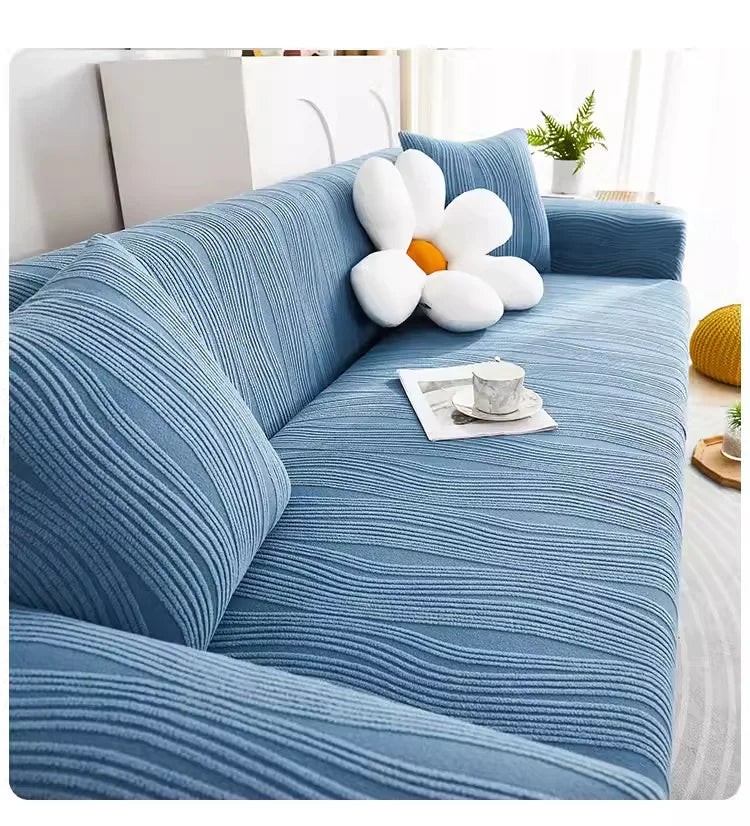 A light blue stretchable sofa cover with vertical ribbing and a white flower cushion on a modern couch.