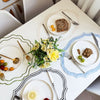 A white table setting with a placemat featuring delicate floral embroidery and various silverware and food items.