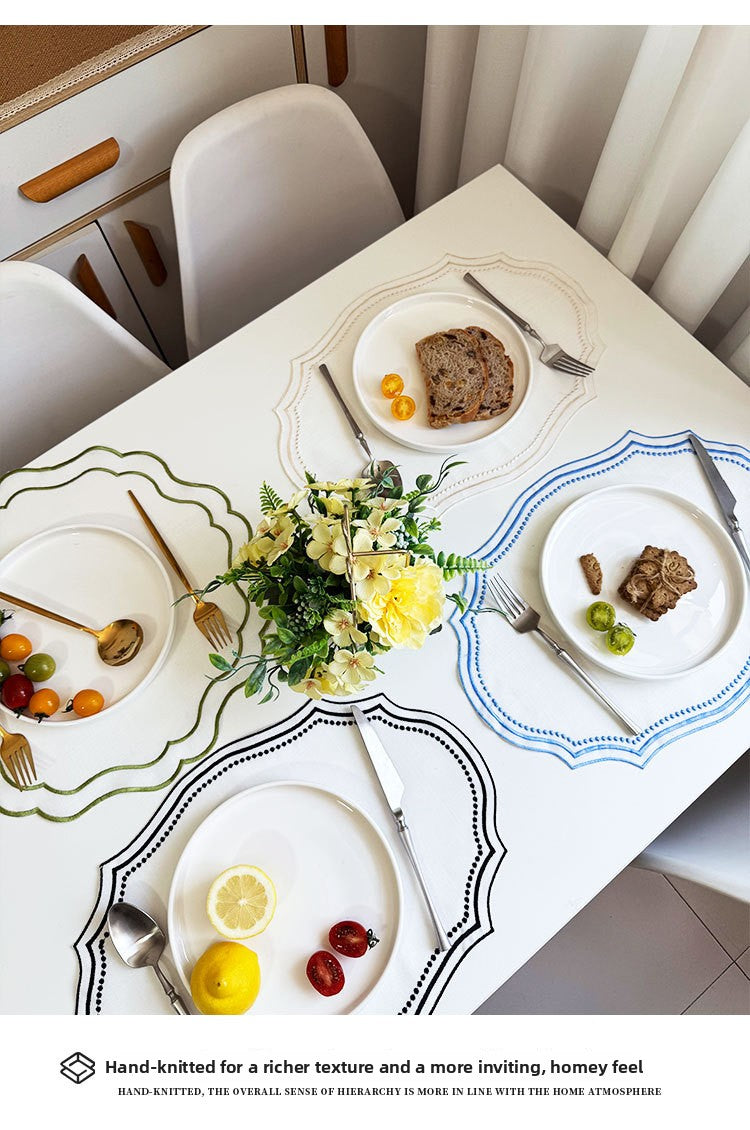 A white table setting with a placemat featuring delicate floral embroidery and various silverware and food items.