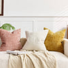 Three throw pillows in pink, cream, and gold textured fabric resting on a light-colored sofa.
