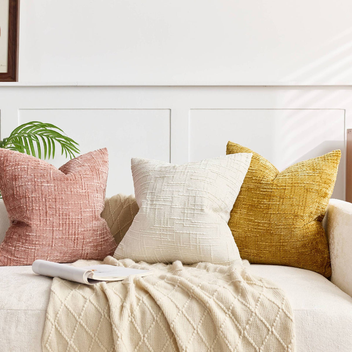 Three throw pillows in pink, cream, and gold textured fabric resting on a light-colored sofa.