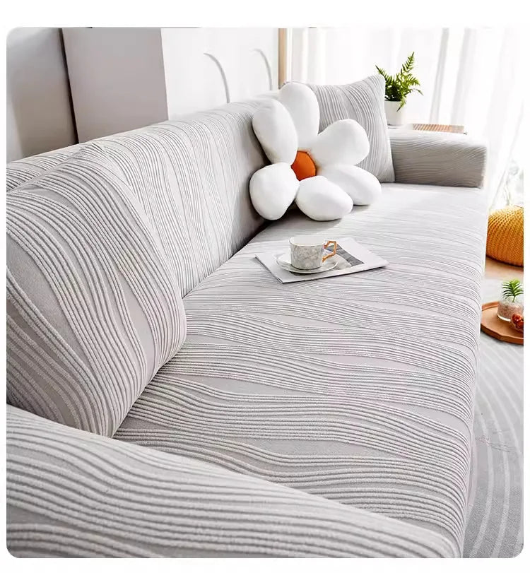 A light gray stretchable sofa cover with white tufted cushions and orange accents in a bright living room setting.