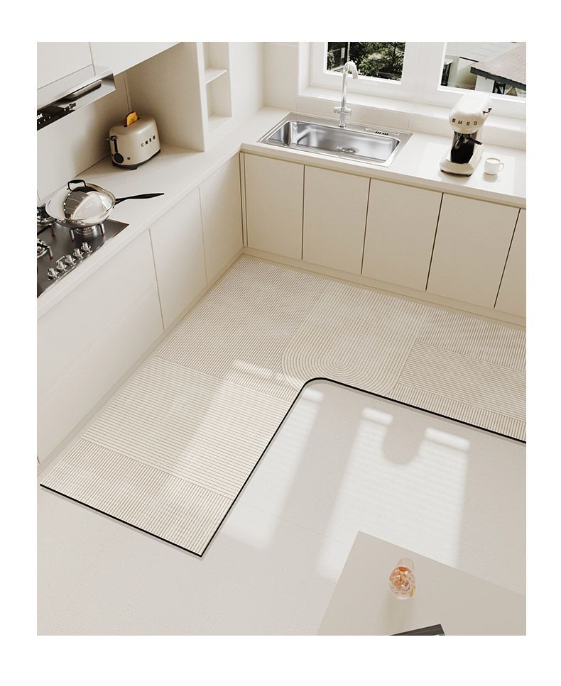 A rectangular beige anti-slip floor mat placed on a light-colored kitchen floor next to white cabinetry and a stainless steel