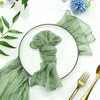 A green rustic gauze table runner is elegantly tied and displayed on a white plate with natural greenery.