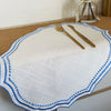 A white cotton linen placemat with blue embroidery and gold cutlery set on a wooden table.