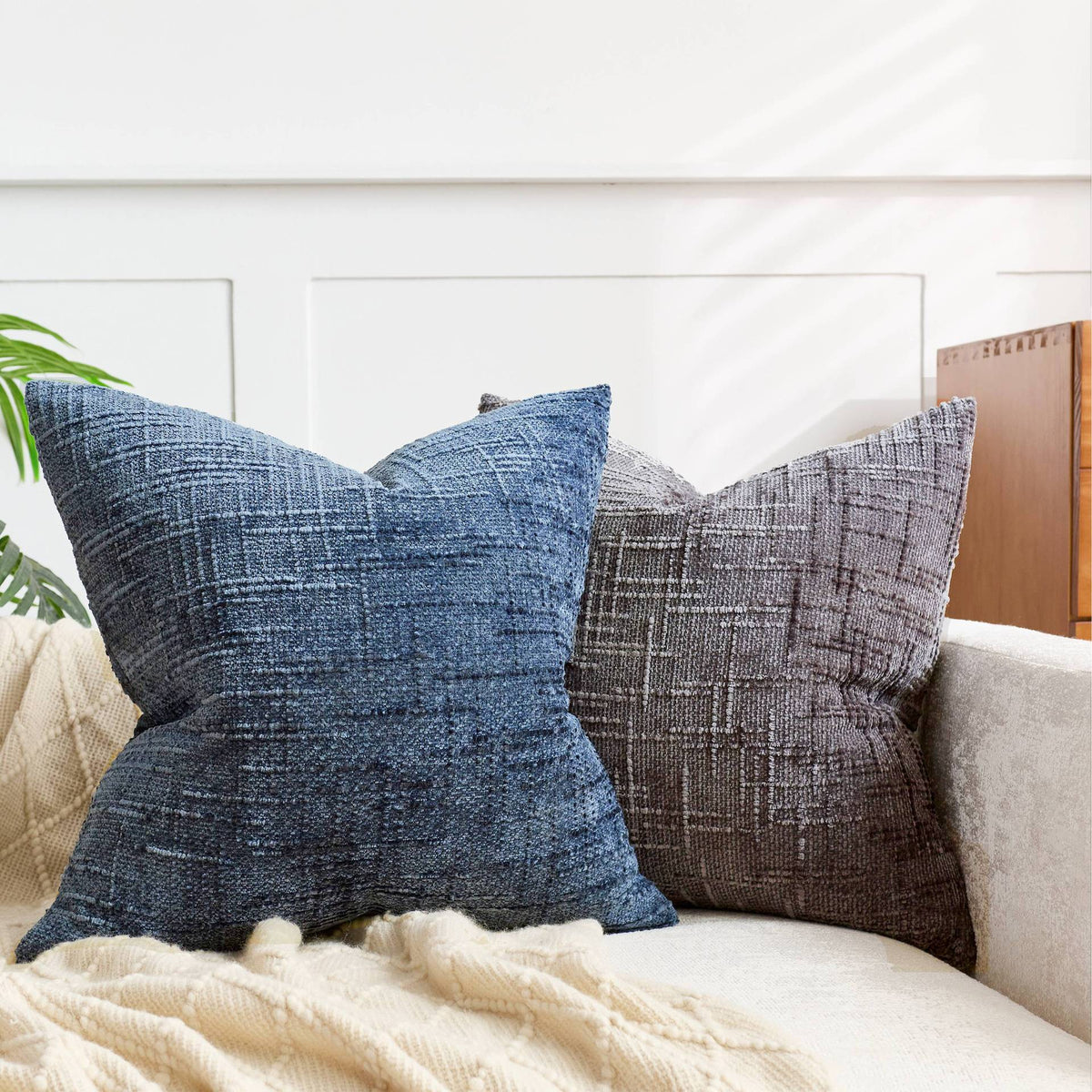 A close-up of a dark blue boucle texture throw pillow resting on a light beige blanket.