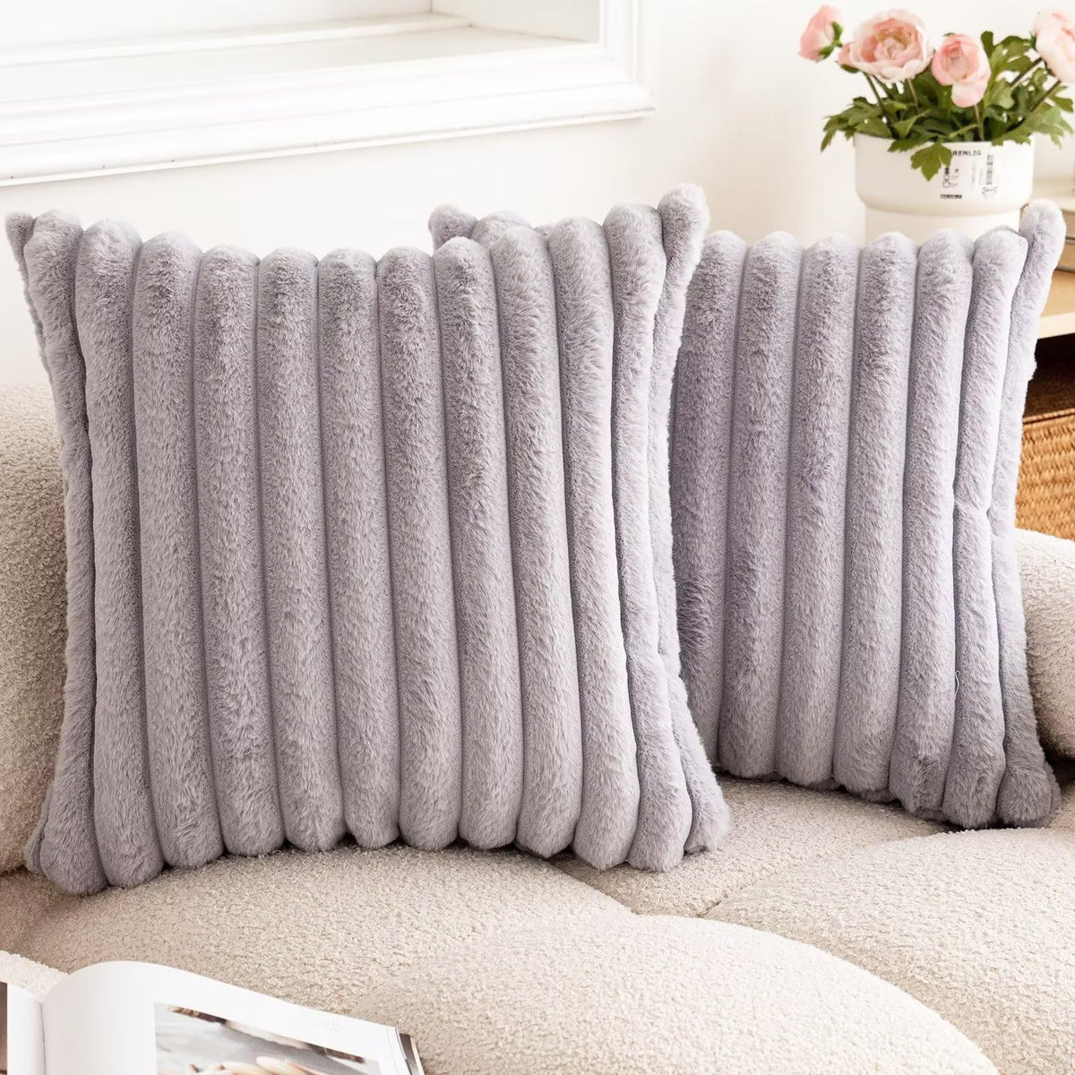 A pair of gray faux rabbit fur cushion covers resting on a light-colored sofa.