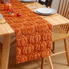 An orange felt table runner decorated with pumpkin shapes is placed on a wooden table.