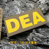 A yellow tactical hook and loop patch labeled DEA is placed on a dark, rough rock surface.