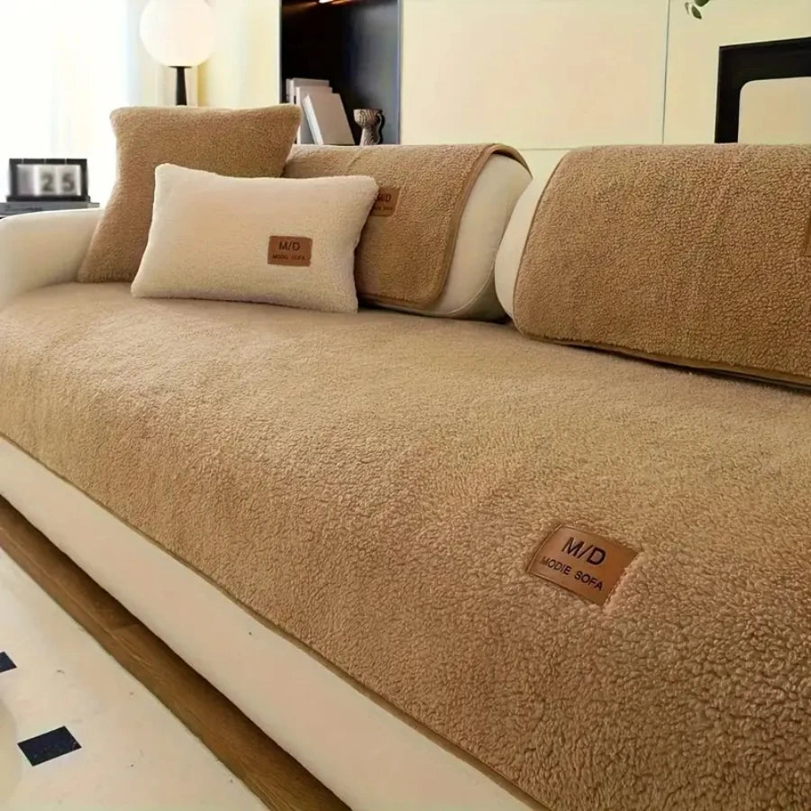 A tan sherpa anti-slip sofa cover with light beige pillows displayed on a modern sofa.