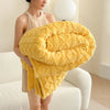 A bright yellow ultra-soft coral fleece blanket is rolled up and draped over a white sofa.