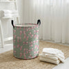 A light green canvas laundry basket with a pink bow pattern sitting on a woven rug.