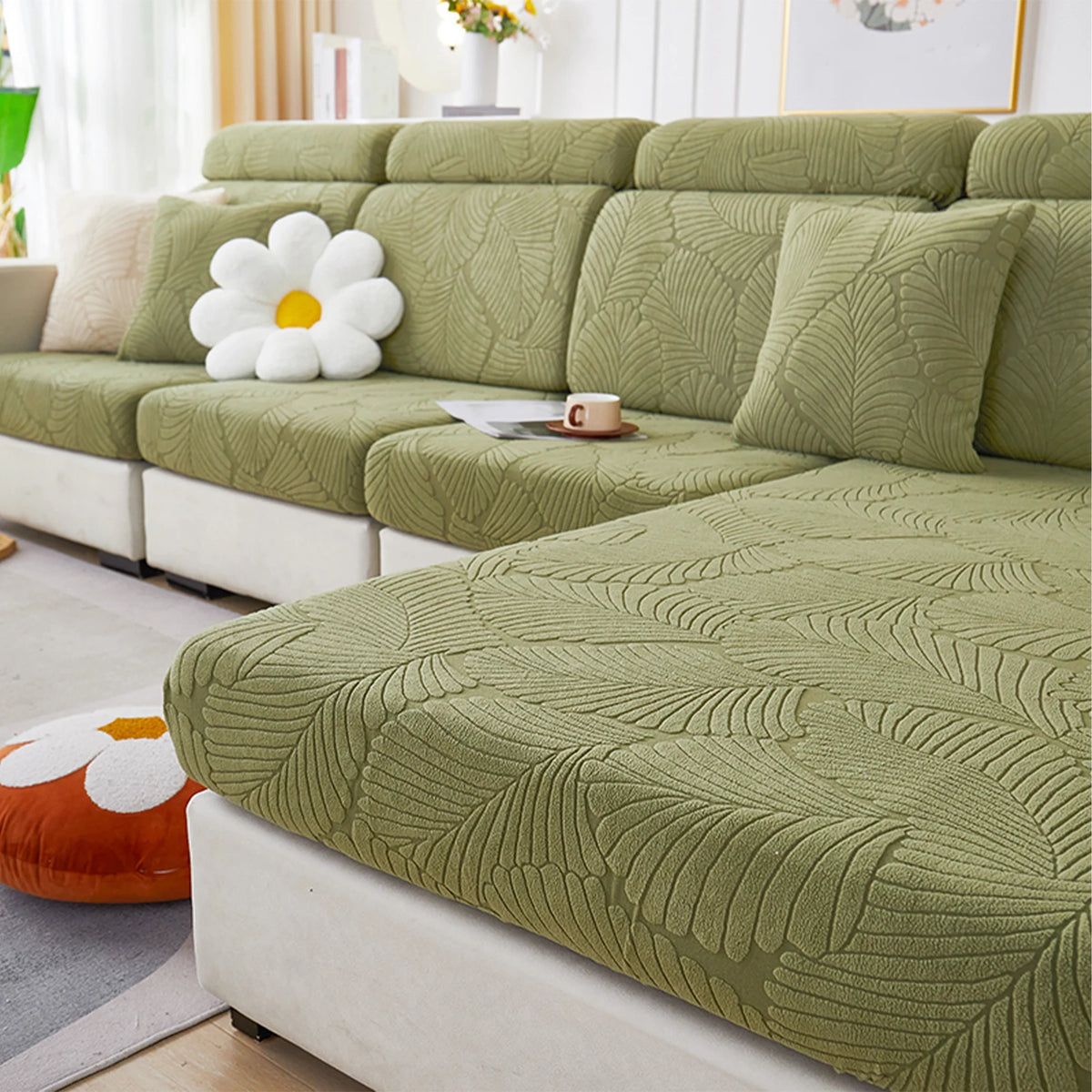 A light olive green leaf jacquard stretch sofa cover with a textured pattern displayed on a modern sofa.