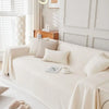 A cream-colored sofa with light beige pillows and a white throw draped on it in a bright living room.
