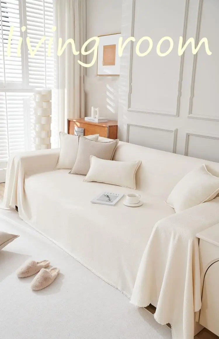 A cream-colored sofa with light beige pillows and a white throw draped on it in a bright living room.