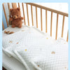 A white quilted silk fabric cooling pillow with small embroidered stars and moons is shown on a wooden crib railing.