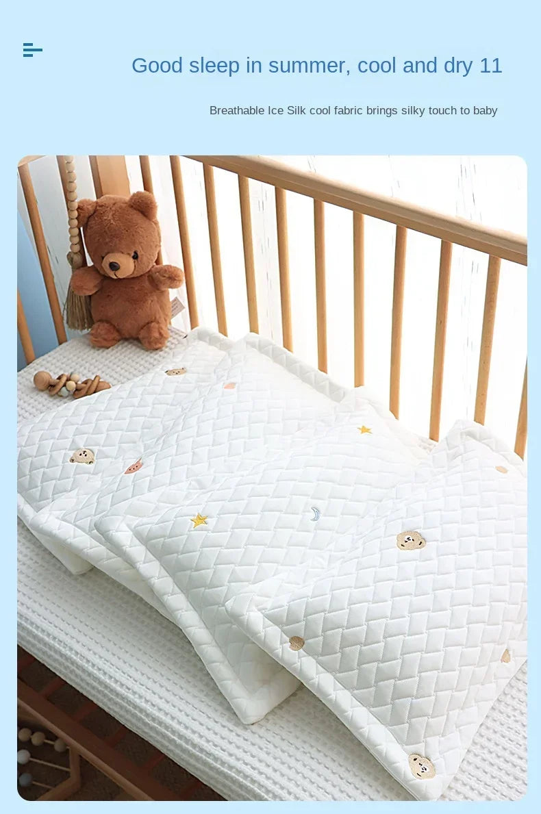 A white quilted silk fabric cooling pillow with small embroidered stars and moons is shown on a wooden crib railing.