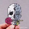 Embroidered skull patch featuring a pink rose and green leaves on a fabric background
