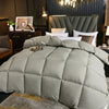 A large, quilted gray goose down comforter is displayed on a bed in a dimly lit room.