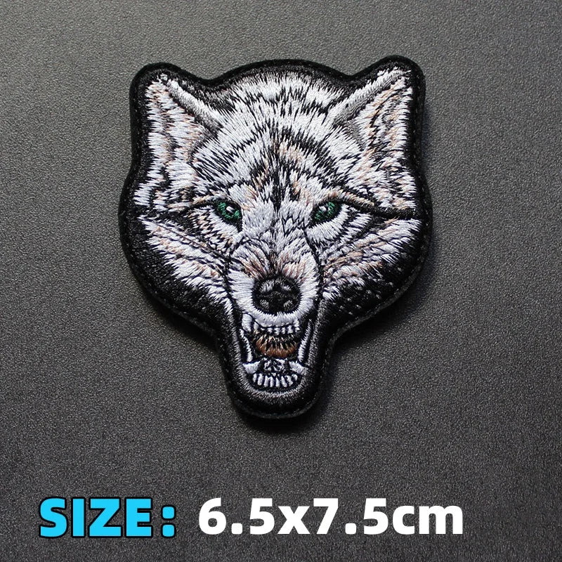 A black and white embroidered patch of a wolf head with green eyes.