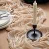 A beige crinkled cheesecloth table runner flows across a wooden surface next to a white candle and silverware.