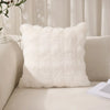 A fluffy white faux rabbit fur decorative throw pillow resting on a light-colored sofa.