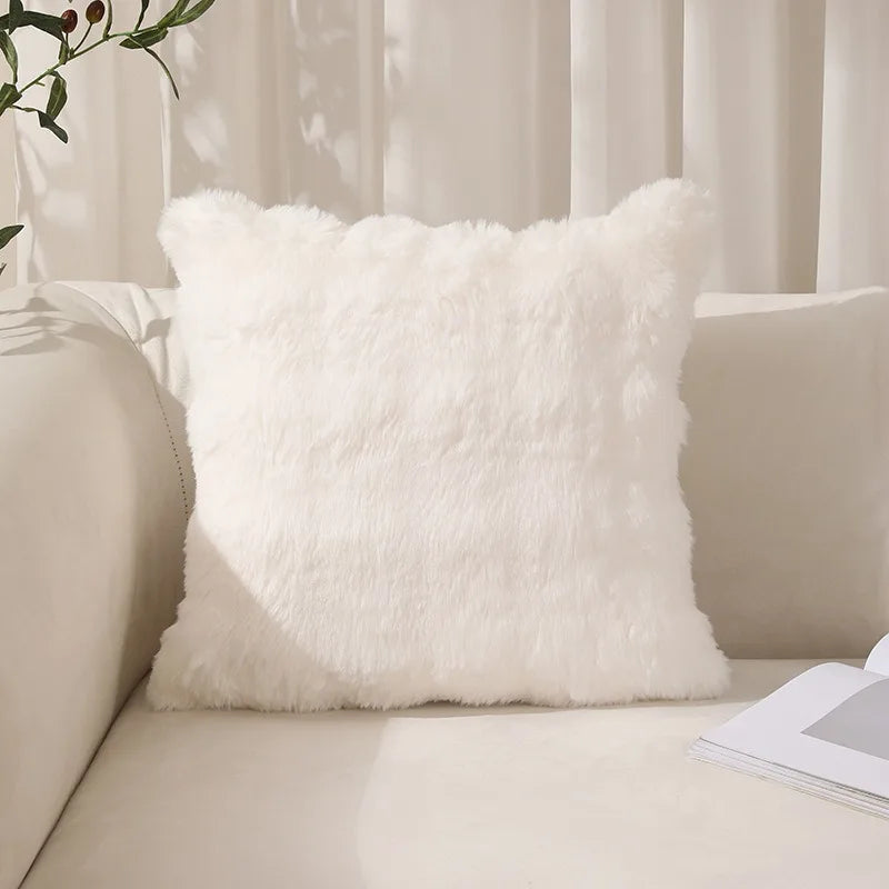 A fluffy white faux rabbit fur decorative throw pillow resting on a light-colored sofa.