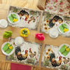 A set of vintage farmhouse rooster placemats featuring detailed illustrations of roosters and floral patterns on wooden table