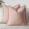 A light pink linen throw pillow with fringe covers resting on a light gray sofa.
