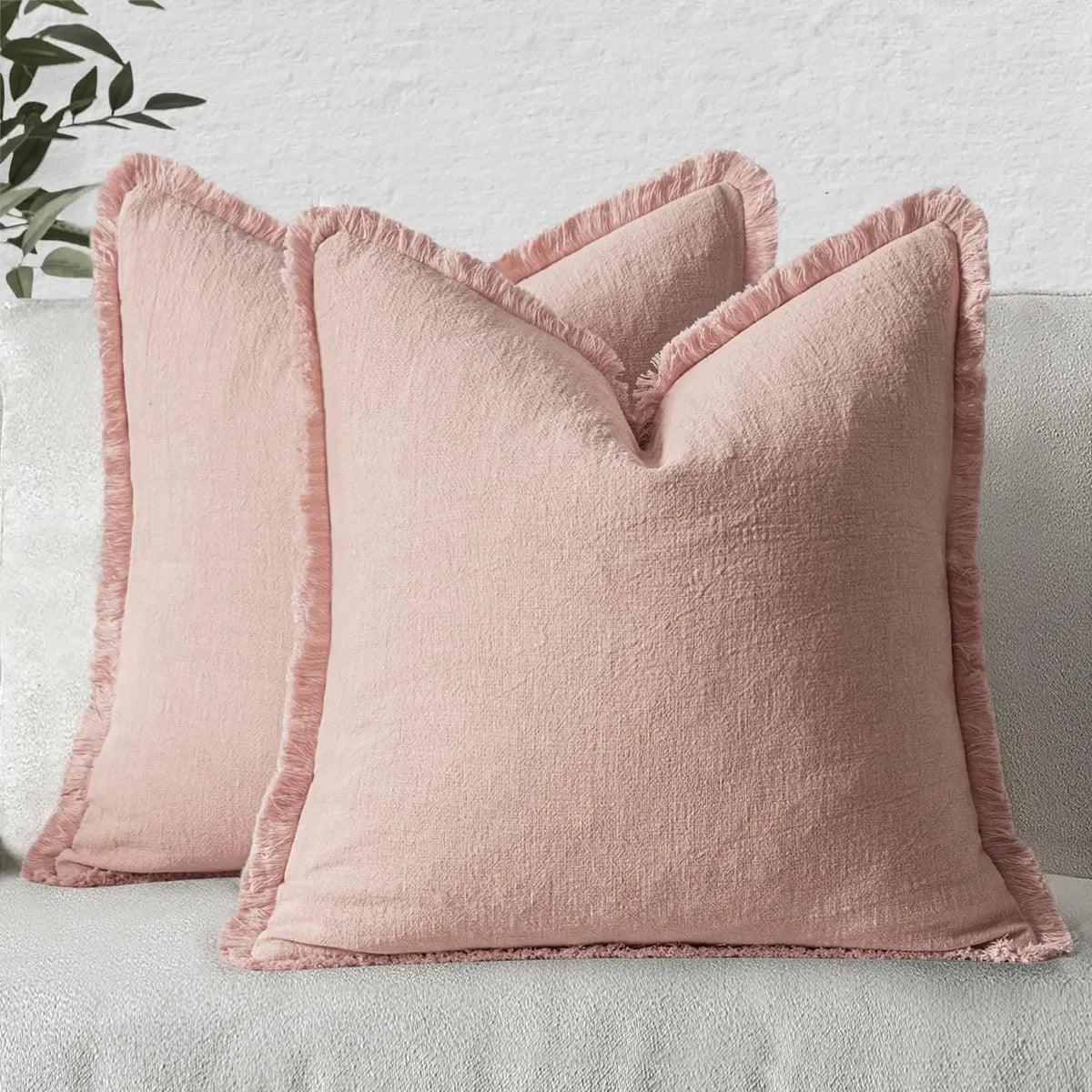 A light pink linen throw pillow with fringe covers resting on a light gray sofa.