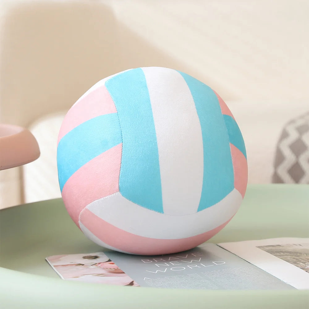 A pink and blue striped plush volleyball ball resting on a light green surface.