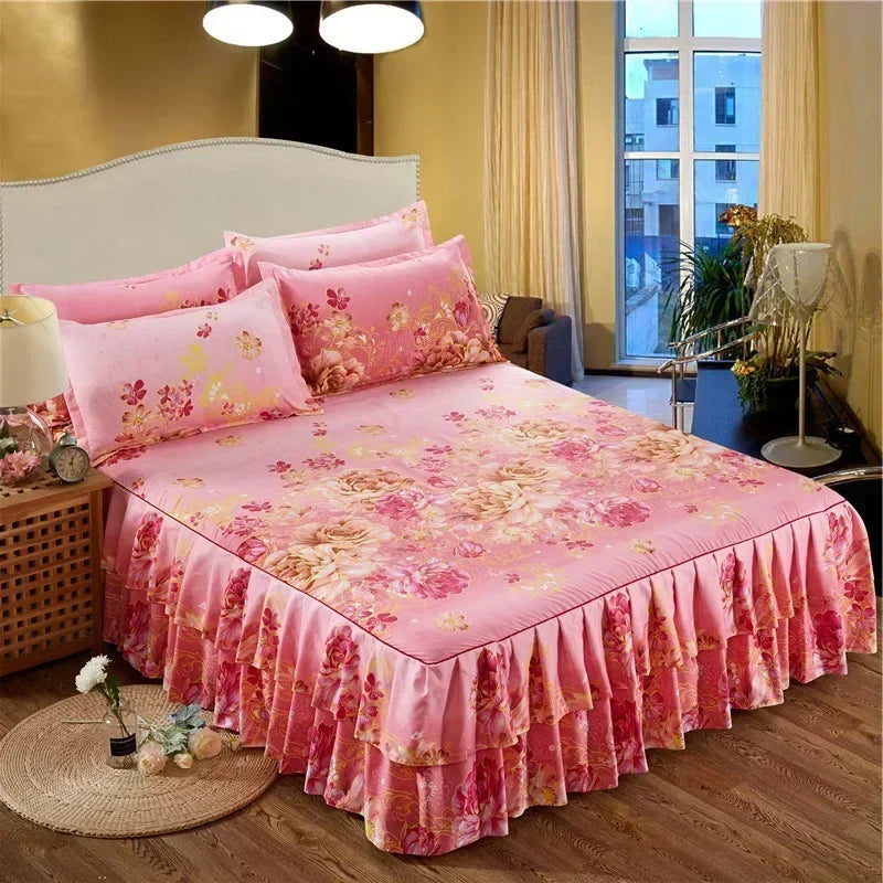 A pink floral printed bed skirt covering a bed with white headboard and sheer curtains.