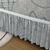 Gray pleated fabric sofa cover with a white trim draped over a wooden floor.