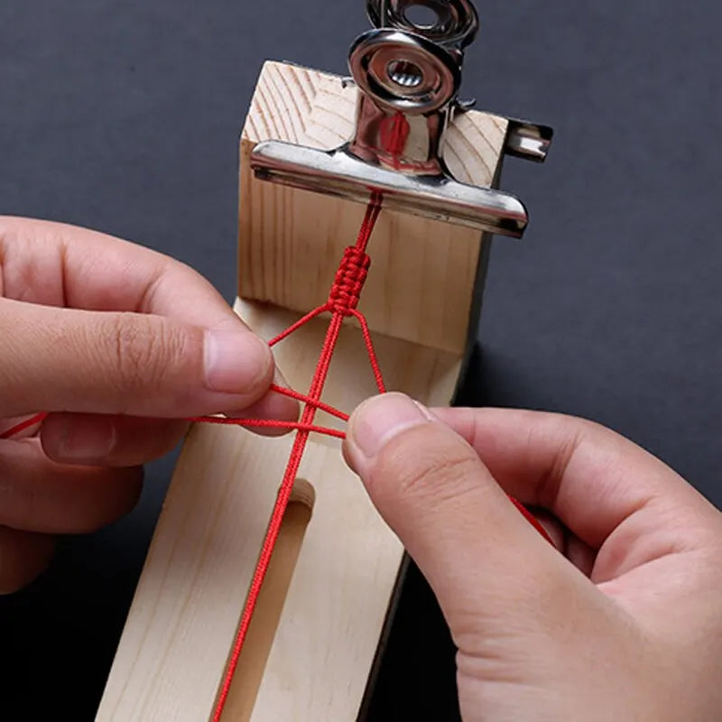 Hands are threading a red cord through a wooden braiding frame for DIY bracelet making.