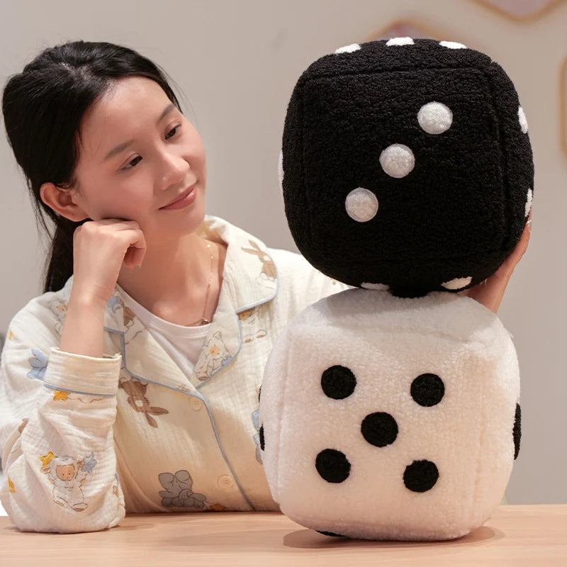 A woman is holding a large, black and white polka-dotted dice plush throw pillow.