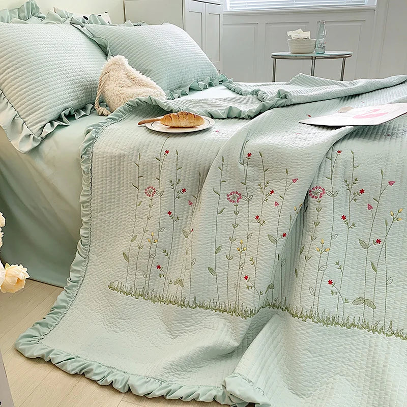 Light mint green floral embroidery quilt bedspread set draped over a bed with white linens.